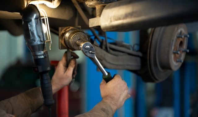 car mechanic worker repairing suspension of lifted automobile at auto repair garage shop station