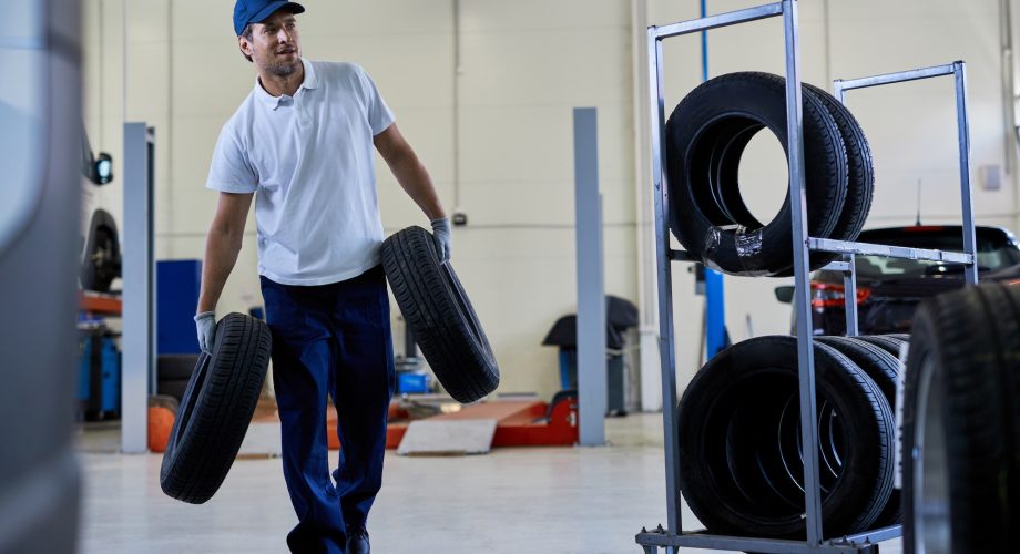 Full length of auto repairman carrying car tires in a workshop.